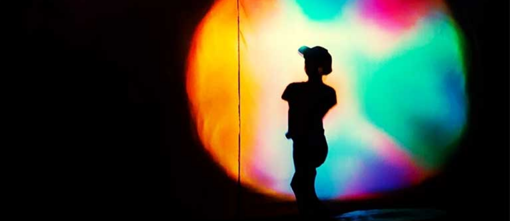 Shadow of a person looking at a colourful light source on a blank wall